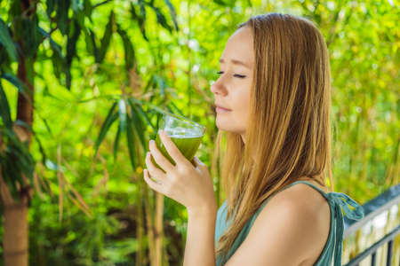 Young woman drinks Celery Juice, Healthy Drink, bunch of celery on a wooden background