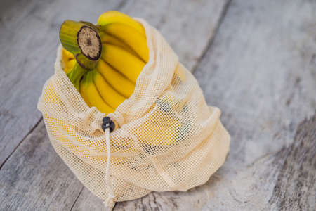 Banana in a reusable bag on a stylish wooden kitchen surface. Zero waste concept, plastic free concept. Healthy clean eating diet and detox. Summer fruitsの写真素材