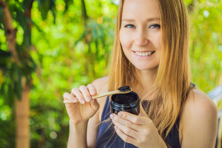 Young woman brush teeth using Activated charcoal powder for brushing and whitening teeth. Bamboo eco brushの写真素材