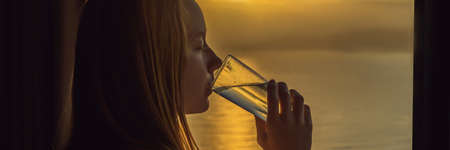 Woman drinks water in the morning on a background of a window with a sea view BANNER, LONG FORMAT