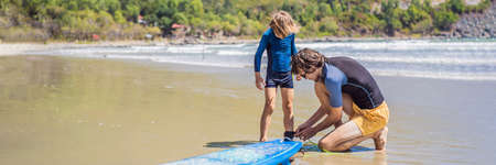 BANNER, LONG FORMAT Father or instructor teaching his son how to surf in the sea on vacation or holiday. Travel and sports with children concept. Surfing lesson for kids.の写真素材