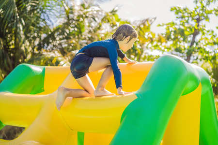 Cute boy runs an inflatable obstacle course in the pool.