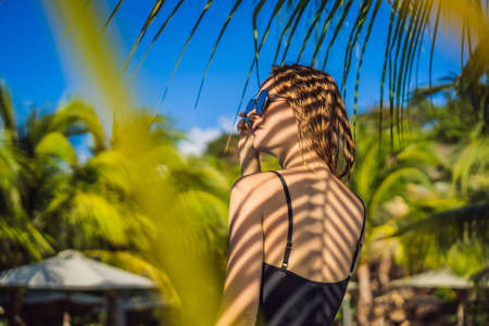 Young woman with the shadow of the palm leaf on her back. Relaxing on the seasideの写真素材