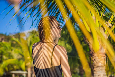Young woman with the shadow of the palm leaf on her back. Relaxing on the seasideの写真素材