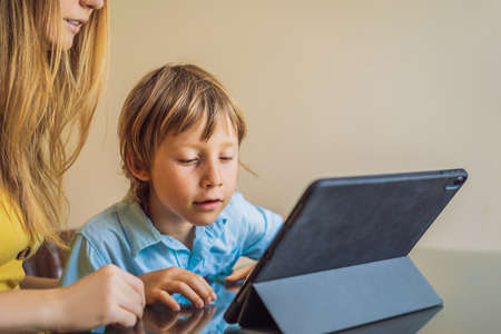 A boy studying online at home using a tablet. Mom helps him learn. Studying during quarantine. Global pandemic covid19 virusの写真素材