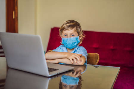 Boy studying online at home using laptop in medical masks to protect against coronovirus. Studying during quarantine. Global pandemic covid19 virusの写真素材