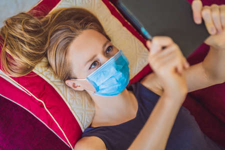 Woman in medical mask reads a book on the couch. Home quarantine. Stay at home. Coronovirus
