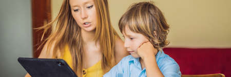 A boy studying online at home using a tablet. Mom helps him learn. Studying during quarantine. Global pandemic covid19 virus BANNER, LONG FORMATの写真素材