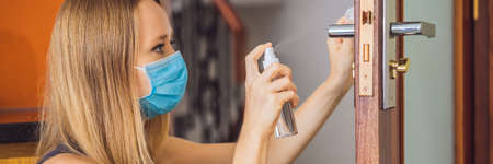 Woman hand is applying sanitizer on the door handle. Cleaning door handle with alcohol spray for...