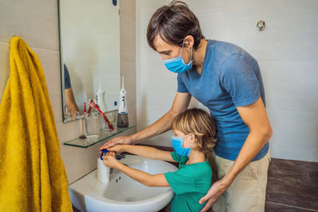 Dad teaches his son to wash his hands properly. Dad and son in medical masks because of coronovirus. Epidemic. Stay home. Wash your handsの写真素材