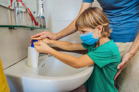 Dad teaches his son to wash his hands properly. Dad and son in medical masks because of coronovirus. Epidemic. Stay home. Wash your handsの写真素材