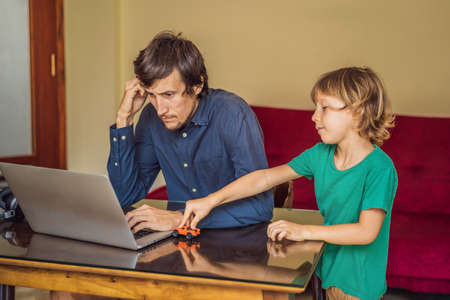 Man is trying to work from home because of the coronovirus epidemic, but his son is stopping him. Self-isolation at home. Children at home schooling. Parents at remote work. Quarantine, self-isolation, coronavirusの写真素材