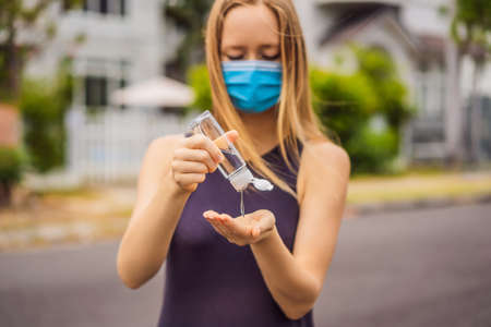 Woman in a small town in a medical mask uses a sanitizer because of a coronovirus epidemicの写真素材