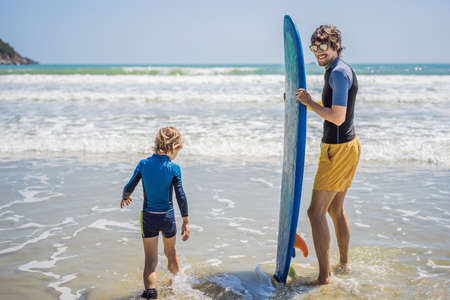 Father or instructor teaching his son how to surf in the sea on vacation or holiday. Travel and sports with children concept. Surfing lesson for kidsの写真素材