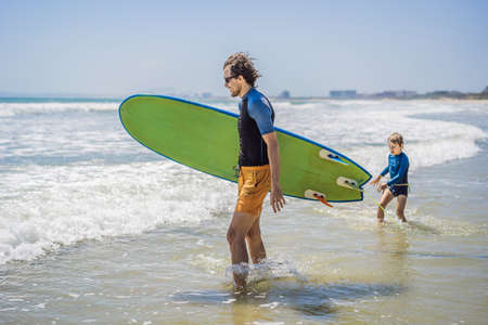 Father or instructor teaching his son how to surf in the sea on vacation or holiday. Travel and...