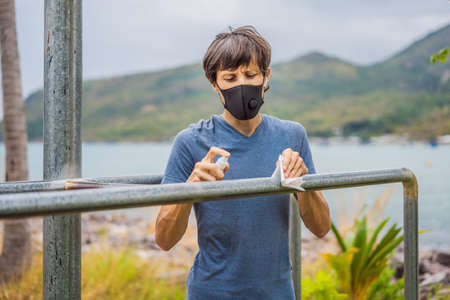 Man disinfects horizontal bar before sports. A man in a medical mask plays sports during the...
