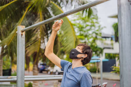 Man disinfects horizontal bar before sports. A man in a medical mask plays sports during the...