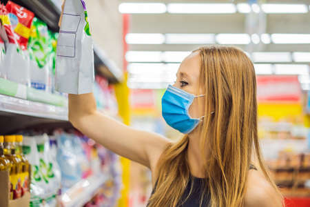 Alarmed female wears medical mask against coronavirus while grocery shopping in supermarket or store- health, safety and pandemic concept - young woman wearing protective mask and stockpiling foodの写真素材
