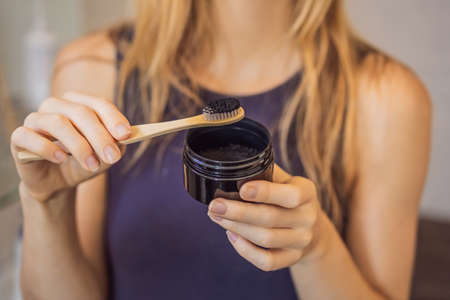 young woman brushing her teeth with a black tooth paste with active charcoal, and black tooth brush in her bathroomの写真素材