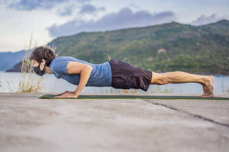 Young man in medical mask performing some workouts in the park during coronavirus quarantine, Coronavirus pandemic Covid-19. Sport, Active life in quarantine surgical sterilizing face mask protection. Outdoor run on athletics track in Corona Outbreakの写真素材