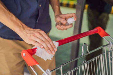 Man hand disinfecting shopping cart with alcohol spray for corona virus or Covid-19 protection