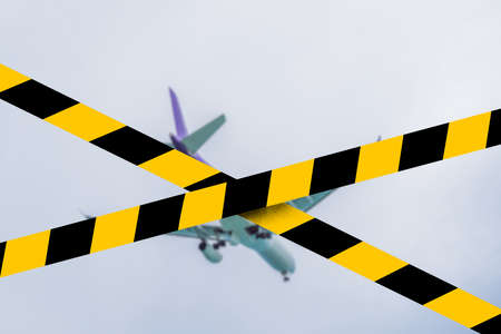Plane in the sky taking off or landing Covid-19 quarantine yellow tape. Coronavirus or 2019-nCov virusの写真素材