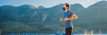 Runner wearing medical mask, Coronavirus pandemic Covid-19. Sport, Active life in quarantine surgical sterilizing face mask protection. Outdoor run on athletics track in Corona Outbreak. Keep your shape during quarantine, pandemic. Young attractive guy in a black medical mask prepares for a jogging in countryside BANNER, LONG FORMATの写真素材