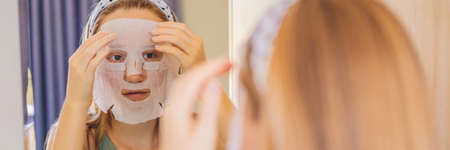 Young red-haired woman doing facial mask sheet. Beauty and Skin Care Concept BANNER, LONG FORMATの写真素材