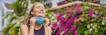 Quarantine is over concept. Woman taking off mask against the background of small town houses. We...