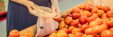 A woman chooses tomatoes in a supermarket without using a plastic bag. Reusable bag for buying vegetables. Zero waste concept BANNER, LONG FORMATの写真素材