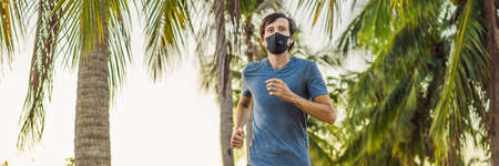 Runner wearing medical mask, Coronavirus pandemic Covid-19. Sport, Active life in quarantine surgical sterilizing face mask protection. Outdoor run on athletics track in Corona Outbreak. Keep your shape during quarantine, pandemic. Young attractive guy in a black medical mask prepares for a jogging in countryside BANNER, LONG FORMATの写真素材