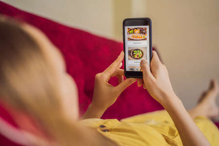 Young woman orders food for lunch online using a smartphoneの写真素材