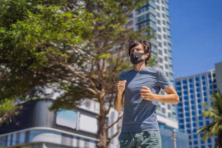 Man runner wearing medical mask. Running in the city against the backdrop of the city. Coronavirus pandemic Covid-19. Sport, Active life in quarantine surgical sterilizing face mask protection. Outdoor run on athletics track in Corona Outbreakの写真素材