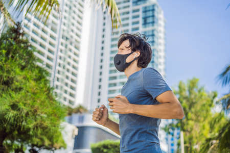 Man runner wearing medical mask. Running in the city against the backdrop of the city. Coronavirus pandemic Covid-19. Sport, Active life in quarantine surgical sterilizing face mask protection. Outdoor run on athletics track in Corona Outbreakの写真素材
