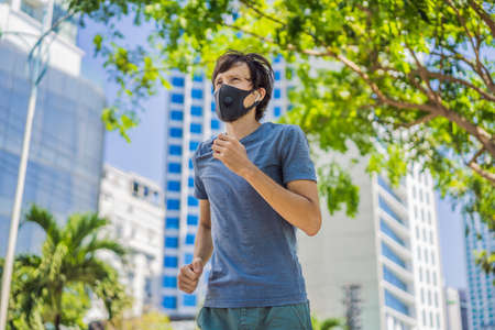 Man runner wearing medical mask. Running in the city against the backdrop of the city. Coronavirus pandemic Covid-19. Sport, Active life in quarantine surgical sterilizing face mask protection. Outdoor run on athletics track in Corona Outbreakの写真素材