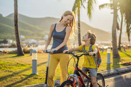 Active school kid boy and his mom riding a bike with backpack on sunny day. Happy child biking on way to school. Safe way for kids outdoors to schoolの写真素材