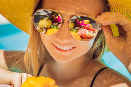 Young woman relaxing and eating fruit plate by the hotel pool. Exotic summer diet. Photo of legs with healthy food by the poolside, top view from above. Tropical beach lifestyleの写真素材