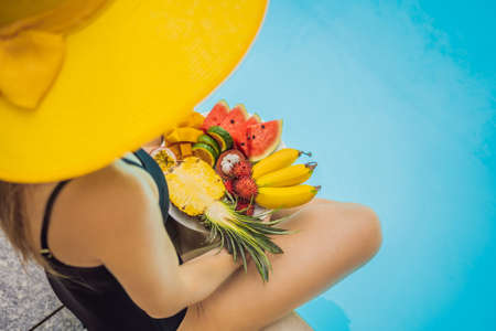 Young woman relaxing and eating fruit plate by the hotel pool. Exotic summer diet. Photo of legs with healthy food by the poolside, top view from above. Tropical beach lifestyleの写真素材