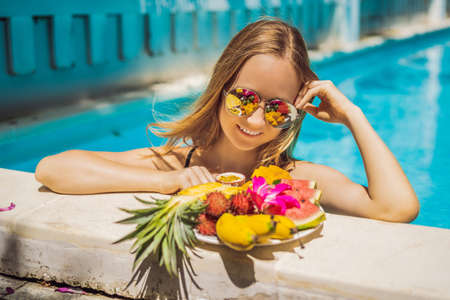 Young woman relaxing and eating fruit plate by the hotel pool. Exotic summer diet. Photo of legs with healthy food by the poolside, top view from above. Tropical beach lifestyleの写真素材