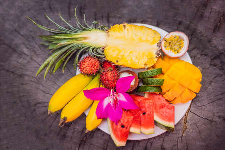 Colorful tropical fruits on big plate. On rustic wooden background. Top viewの写真素材