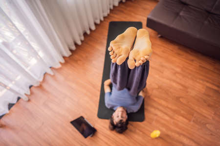 Fitness man exercising on the floor at home and watching fitness videos in a tablet. People do...
