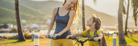 Active school kid boy and his mom riding a bike with backpack on sunny day. Happy child biking on way to school. Safe way for kids outdoors to school BANNER, LONG FORMATの写真素材