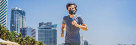 Man runner wearing medical mask. Running in the city against the backdrop of the city. Coronavirus pandemic Covid-19. Sport, Active life in quarantine surgical sterilizing face mask protection. Outdoor run on athletics track in Corona Outbreakの写真素材