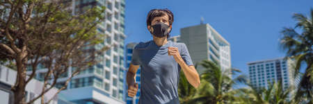 Man runner wearing medical mask. Running in the city against the backdrop of the city. Coronavirus pandemic Covid-19. Sport, Active life in quarantine surgical sterilizing face mask protection. Outdoor run on athletics track in Corona Outbreakの写真素材