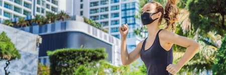 Woman runner wearing medical mask. Running in the city against the backdrop of the city. Coronavirus pandemic Covid-19. Sport, Active life in quarantine surgical sterilizing face mask protection. Outdoor run on athletics track in Corona Outbreakの写真素材