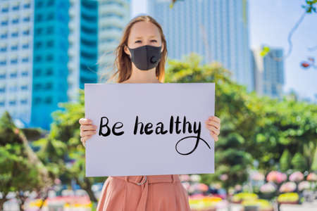 woman in medical mask prevents coronavirus disease holds a poster BE HALTHY Hand written text - lettering isolated on white. Coronovirus COVID 19 conceptの写真素材