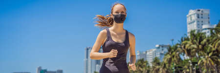 Woman runner wearing medical mask. Running in the city against the backdrop of the city. Coronavirus pandemic Covid-19. Sport, Active life in quarantine surgical sterilizing face mask protection. Outdoor run on athletics track in Corona Outbreakの写真素材