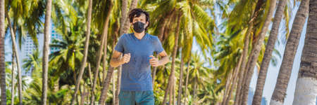 Man runner wearing medical mask. Running in the city against the backdrop of the city. Coronavirus pandemic Covid-19. Sport, Active life in quarantine surgical sterilizing face mask protection. Outdoor run on athletics track in Corona Outbreakの写真素材