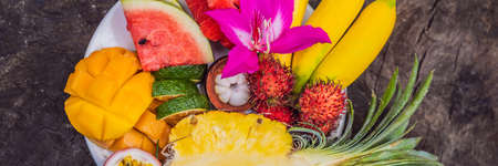Colorful tropical fruits on big plate. On rustic wooden background. Top view BANNER, LONG FORMAT