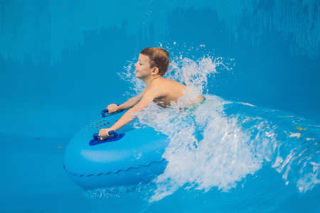 Boy on a pool float on artificial waves in a water park